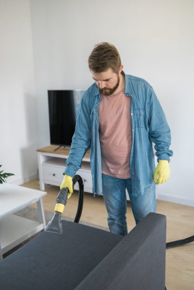 Professional cleaner cleaning a residential sofa with a vacuum and detergent.